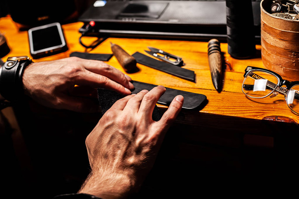 Man maakt een leder product, en poliert het in een thuis workshop. Op een houten tafel. - Foto, afbeelding