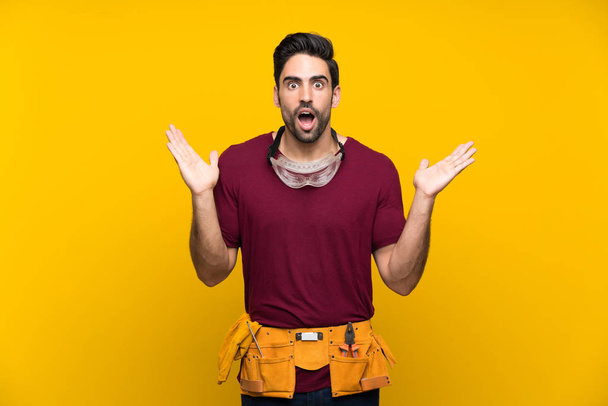 Handsome young craftsman over isolated yellow background with shocked facial expression - Photo, Image