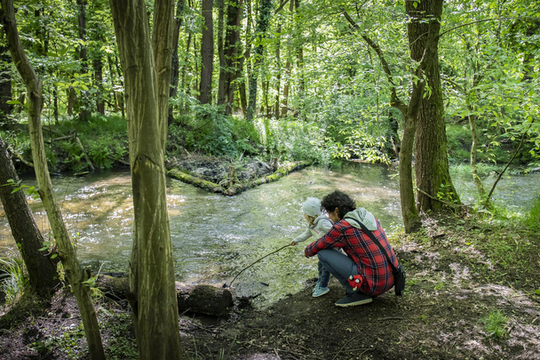 Joven papá y niño jugando cerca de un arroyo en bosques verdes
 - Foto, imagen