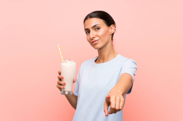 Молодая женщина с клубничным молочным коктейлем на изолированном розовом фоне указывает пальцем на вас с уверенным выражением
 - Фото, изображение