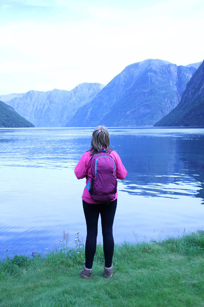 girl with a backpack on her back looks at the mountains and the Norwegian fjords - Foto, afbeelding