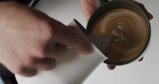 Barista Ρίχνει γάλα σε φλιτζάνι εσπρέσο για να κάνει Latte Art close-up. Επαγγελματική καφετιέρα σχέδιο Latte ή Cappuccino τέχνη για καφέ με γάλα σόγιας. Διαδικασία παρασκευής λακτόζης δωρεάν ποτό στο καφέ  - Πλάνα, βίντεο