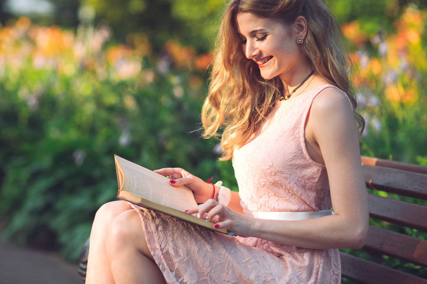 Nuori tyttö lukee kirjaa, joka istuu penkillä auringonlaskun aikaan.
 - Valokuva, kuva