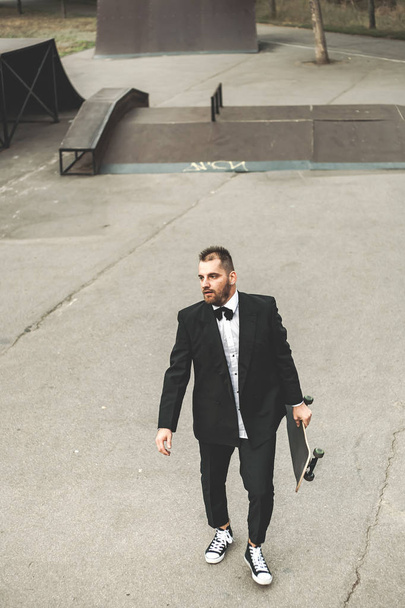 A guy in a classic black suit. Skateboarding, free life concept. - Photo, image