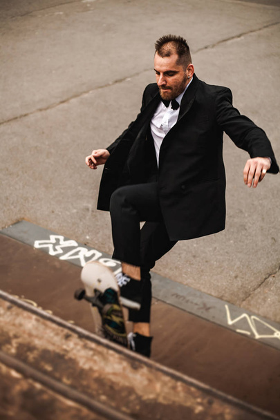 A guy in a classic black suit. Skateboarding, free life concept. - Foto, afbeelding