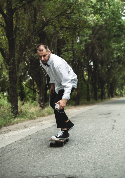 A guy in a classic black suit. Skateboarding, free life concept. - Zdjęcie, obraz