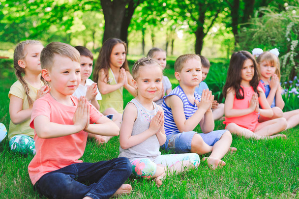 Duża grupa dzieci zaangażowanych w jogę w parku siedzi na trawie - Zdjęcie, obraz