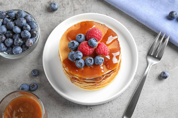Tasty pancakes with fresh berries and syrup served on grey table, above view - Foto, Imagen