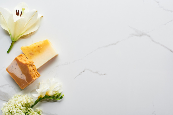 top view of natural soap pieces near fresh flowers on marble surface - 写真・画像