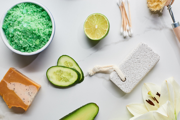 вид на зеленые соли для ванн, мыло и пемзу рядом со свежим цветком, известью и огурцом на мраморной поверхности
 - Фото, изображение