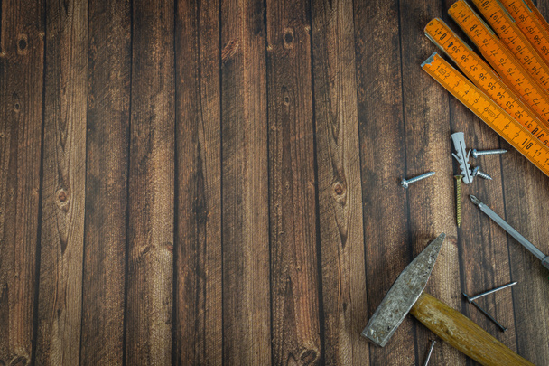 Handgereedschap op een donkere houten ondergrond, hamer met spijkers en een klapregel, ernaast een schroevendraaier met verschillende schroeven en tangen - Foto, afbeelding