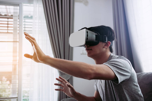 Young asian man wearing virtual reality glasses at living room f - Фото, изображение