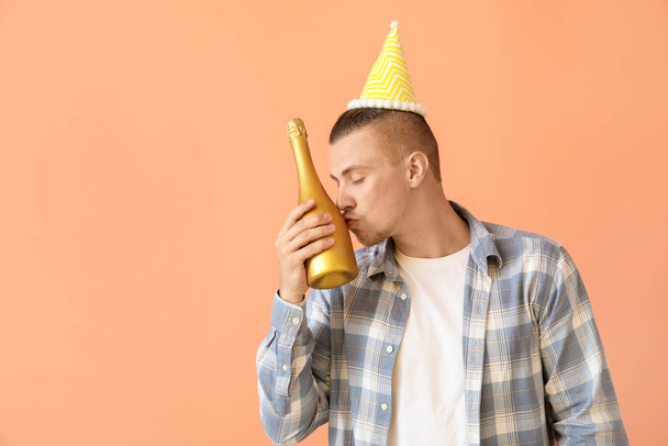 Drunk man with party hat and bottle of champagne on color background - Photo, Image