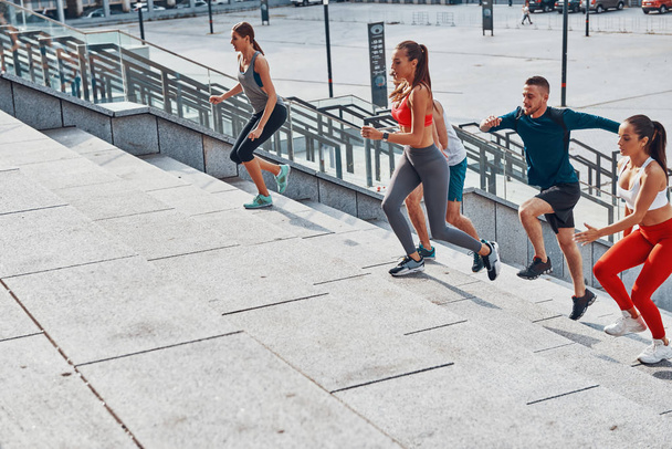 Group of young people in sports clothing jogging on concrete stairs up in city  - Fotografie, Obrázek