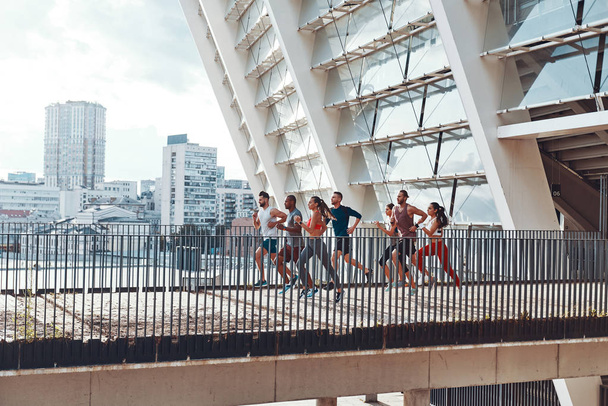 friends in sports clothing jogging on bridge outdoors in city with buildings and houses  - Fotó, kép