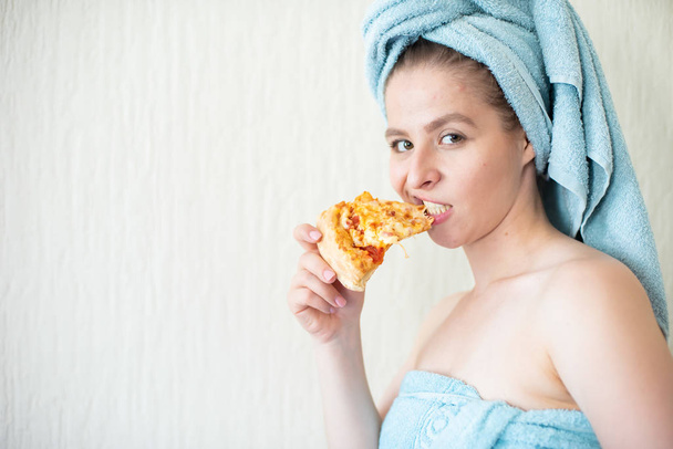 Cute girl with a towel on her head eats pizza in bed. Portrait of a young woman eating fast food in bed. Bodypositive - Zdjęcie, obraz