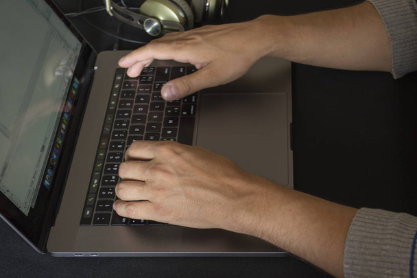 Hands pushing buttons on laptop keyboard and headphones lying nearby on a black table background. - Photo, image
