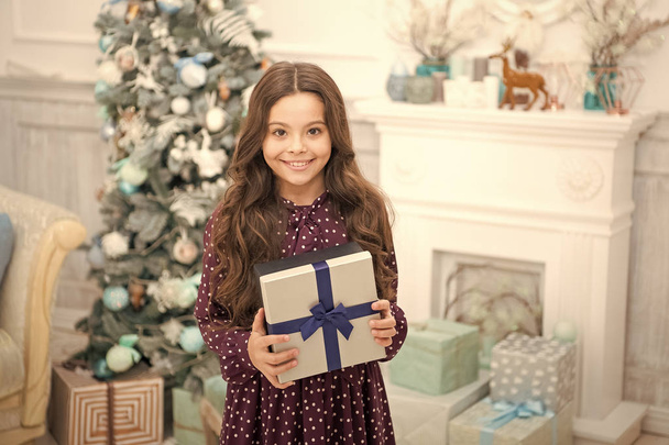 Christmas is coming. Small cute girl received holiday gift. Best christmas gifts. Child excited about unpacking her gift. Kid little girl in elegant dress and gift box christmas tree background - Foto, afbeelding