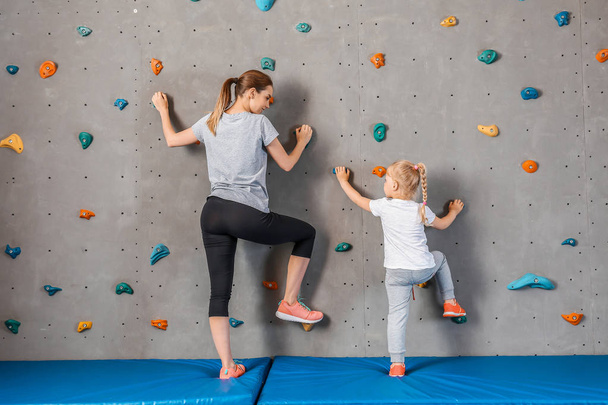 Young woman with her little daughter climbing wall in gym - Фото, зображення