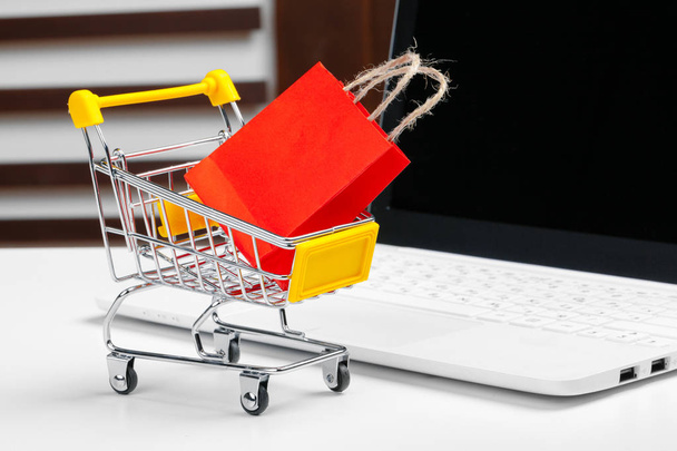 Online nákupní koncept. Nákupní košík, laptop na stole - Fotografie, Obrázek