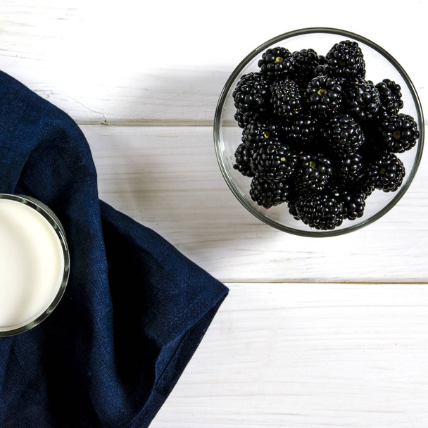 Black blackberries and a glass of milk stand on a white wooden table. Village style - Foto, Bild
