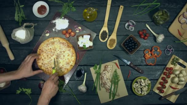 Cheese pizza on ecological black background.Man cuts a slice of pizza and takes it. Pizza consists of ingredients: different sheese, spices and tomatoes. There are many other products on table for cooking and eating pizza. - Footage, Video