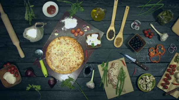 生態学的な黒の背景にチーズピザ。ストップモーション.チーズピザは、エコブラックテーブルの上で単独で旋回しています。ピザは、食材で構成されています:異なるシーズ、スパイス、トマト。ピザを調理し、食べるためのテーブルの上に他の多くの製品があります. - 映像、動画