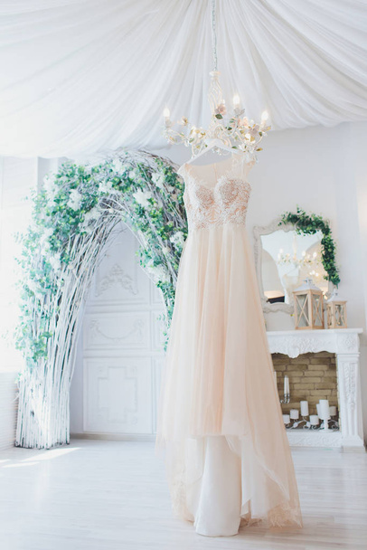 Rich pink wedding dress hangs on a chandelier in a white room. - Foto, afbeelding
