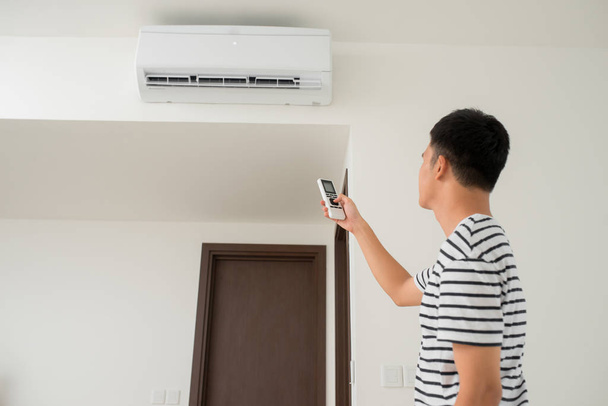 Air conditioner inside unit with man operating remote controller. / Air conditioner with remote controller - Photo, Image