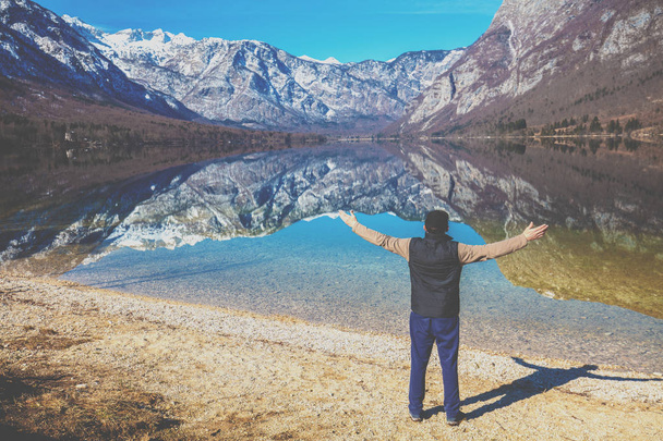 Man with hands in the air standing on the shore of the mountain lake in early spring. Bohinj lake, Slovenia, Europe - Foto, imagen