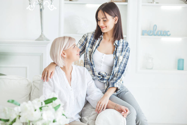 Mature mother and her adult daughter together. Women indoors portrait. Middle age woman and her daughter at home sitting on the couch. - Foto, Imagen