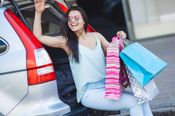 Young attractive woman after shopping. Female putting her shopping bags into the car. Cheerful lady at shopping mall. - Photo, image