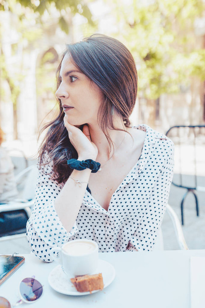 довольно серьезная и вдумчивая женщина ждет во время питья кофе на террасе в городе
 - Фото, изображение