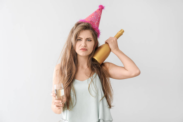 Drunk woman with party hat and champagne on light background - Valokuva, kuva