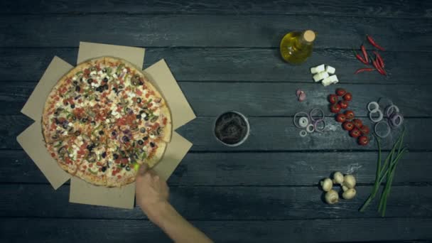 Wegetariańska Pizza na ekologicznym czarnym tle. Człowiek tnie pizzę następnie bierze szklankę piwa i kawałek pizzy. Pizza z różnymi napełniania: pomidory, papryka, grzyby, różne sery, oliwki. Istnieje wiele innych produktów na stole do jedzenia pizzy. - Materiał filmowy, wideo