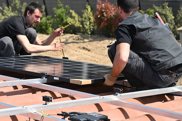 Bouwvakker installeert alternatieve energie fotovoltaïsche zonnepanelen op dak van individuele woning - Foto, afbeelding