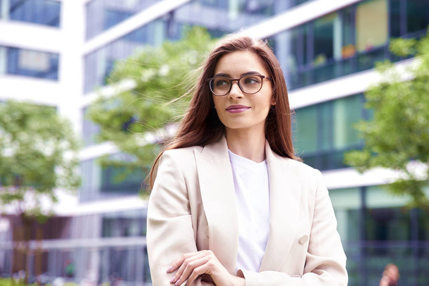 Shot of beautiful young businesswoman wearing blazer and eyeglasses while standing on the street with folded arms.  - Photo, Image