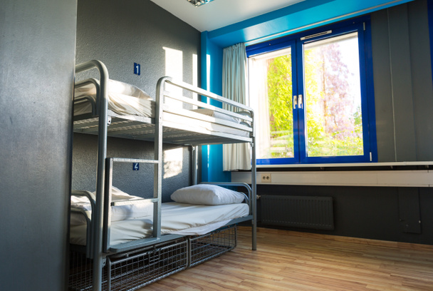 Hostel interior, metal bunk beds and linen, nobody. Empty sleep motel room, dorm bedroom for travelers and tourists - Foto, Imagem