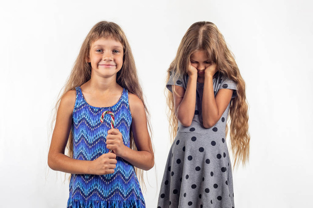 Mädchen hält freudig Bonbons in der Hand, trauriges anderes Mädchen im Hintergrund - Foto, Bild