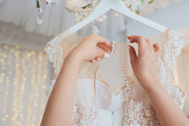 Rich pink wedding dress hangs on a chandelier in a white room. - Foto, Bild