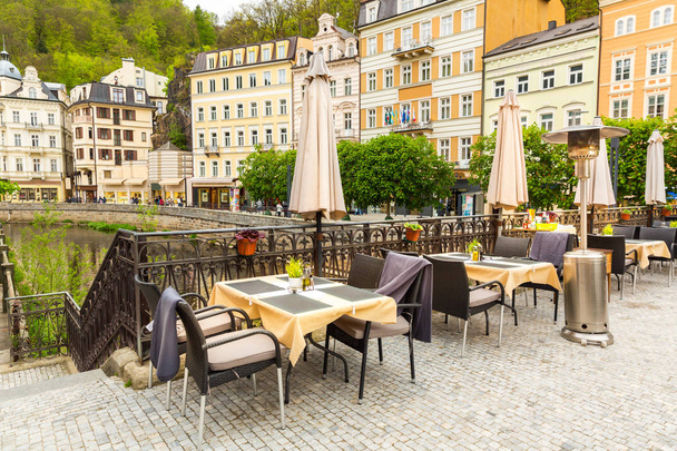 Cosy outdoor cafe with rattan furniture and view on river, Karlovy Vary, Czech Republic, Europe. Old european town, famous place for travel and tourism - Photo, Image