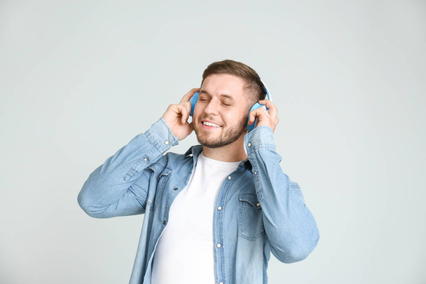 Handsome young man listening to music on light background - Zdjęcie, obraz