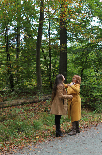 two people, mother and daughter, a woman and a young girl hold hands, talk in a yellow autumn park, throw up fallen leaves, the concept of family relationships, generations - Foto, imagen