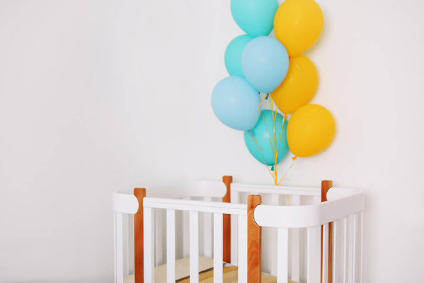Baby bedroom interior. Minimalistic baby room interior. Festive balloons in front of baby bed. Baby birthday celebration concept.  - Foto, immagini