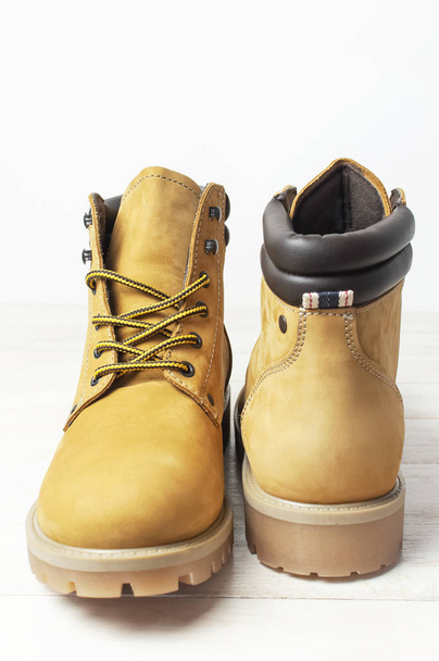 Zbliżenie żółte męskie buty robocze z naturalnej skóry Nubuk na drewnianym białym tle. Modny styl casual obuwie młodzieżowe. Koncepcja reklamy jesień buty zimowe sklep sprzedaży - Zdjęcie, obraz