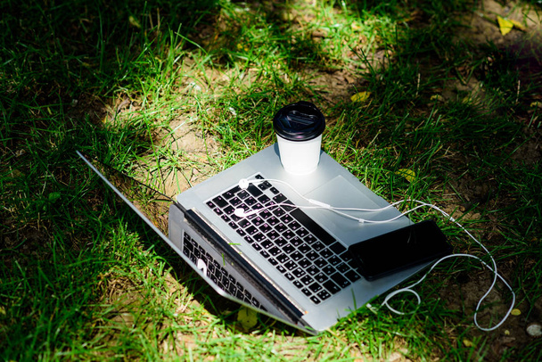 laptop with headset of mobile phone and coffee to go on green grass. agile business. Online study. summer vibes. Relax. university students life. Online shopping. working place outdoor. Free music - Photo, image