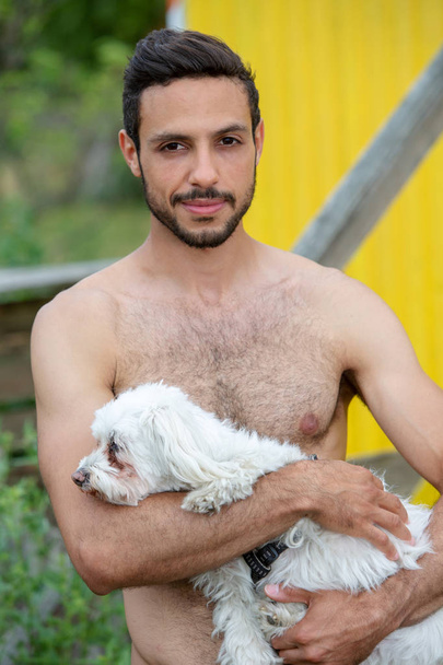 portrait of handsome shirtless man holding a white little dog - Fotoğraf, Görsel