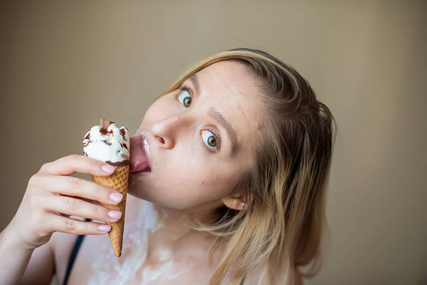 Sexy blonde licks a waffle cone. Ice cream is melting, erotically draining through the body of an attractive woman. Beautiful girl smeared with ice cream. - Zdjęcie, obraz