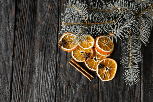 naranja en rodajas secas con un palo de canela y una ramita de abeto en un tablero negro
 - Foto, imagen