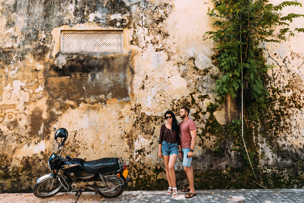 The couple travels on a scooter in Sri Lanka. Man and woman traveling. The couple travels to Asia. Independent travel on motorcycle. Man and woman at the old wall - Foto, Bild